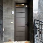 桃園平鎮C9B-2069現代玄關門實際安裝案例，簡約平板門面搭配立體不鏽鋼管線條，以FR-81255G深色烤漆呈現俐落幾何層次，上方搭配開天設計，適合現代住宅玄關大門。