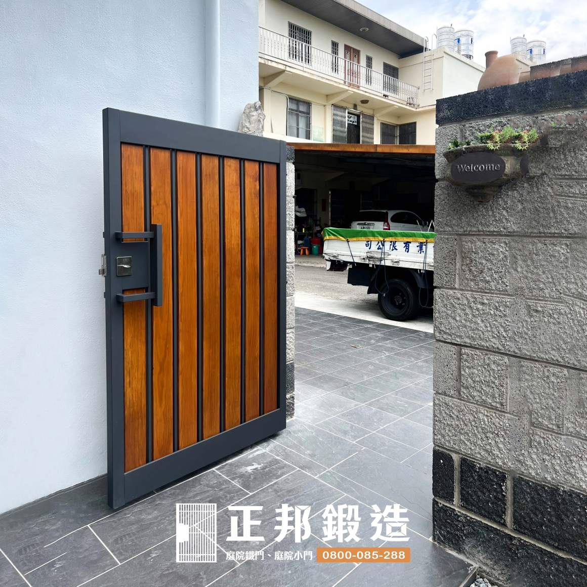 頭份庭院門側面完工實景，FR-2910M1深灰色不鏽鋼框架呼應住宅既有灰色石材門柱，中間搭配橡木色南方松增加溫暖層次，使庭院大門在不同觀看角度下都能與白色外牆、石材及戶外植栽自然融合
