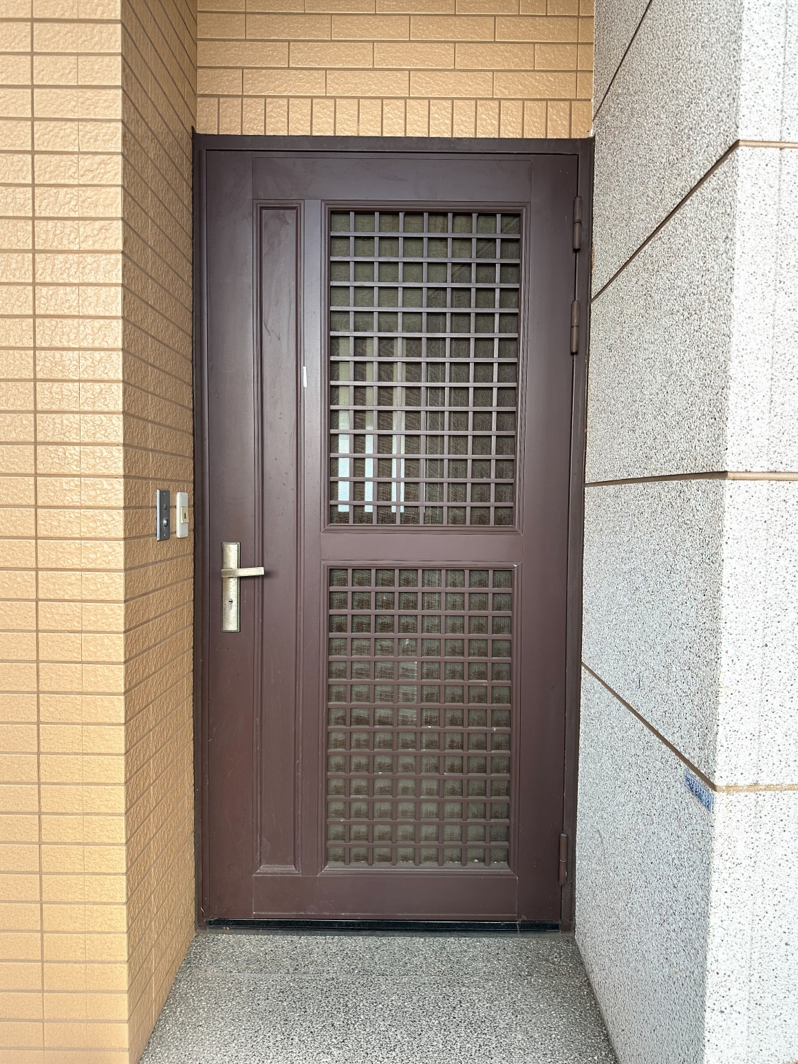 台中老屋翻新換大門前現況，住宅外側原有咖啡色金屬格柵鐵門，門體仍可使用但造型與使用方式已帶有明顯年代感，正邦於包框換門前先確認入口、舊門框及周邊磁磚條件。