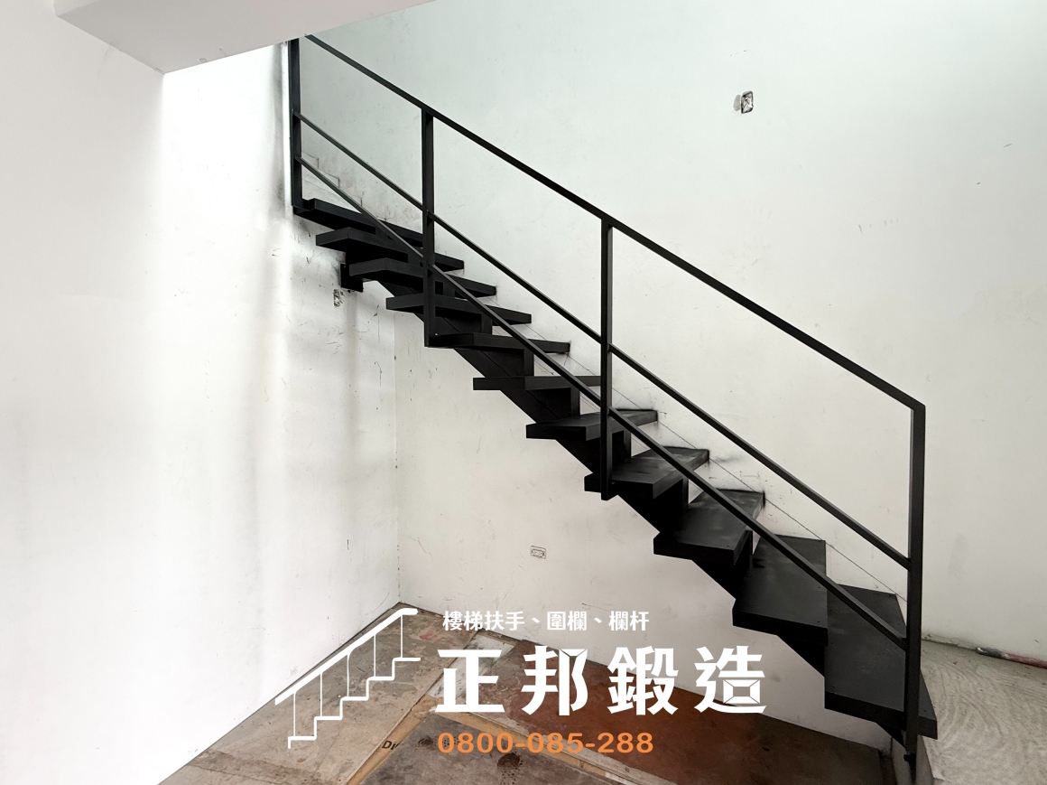 正邦鍛造南投住宅黑色龍骨梯側面全景，從較遠視角可見整段鋼構梯身沿牆面連接上下樓層，踏階下方保留完整的開放區域，外側鐵件扶手採水平線條搭配直立支柱。照片能同時觀察樓梯占用的視覺範圍、下方可使用地坪，以及龍骨梯在未完成室內裝修環境中的實際樣貌。