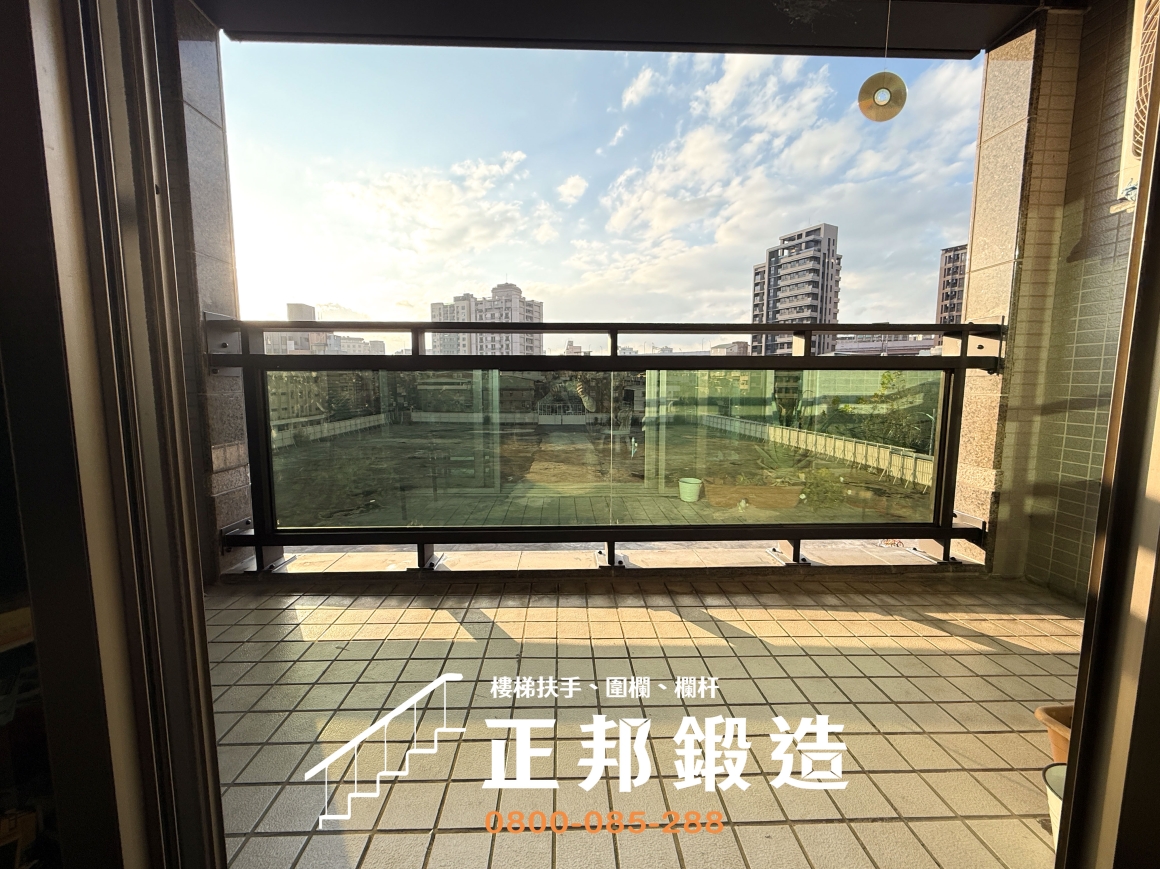 正邦鍛造台北松隆路C9F-1015不鏽鋼玻璃欄杆完工實拍，從陽台室內向外拍攝完整黑色橫向骨架與大面積綠半反射強化玻璃，使用9637黑消光烤漆，與原有陽台磁磚及外牆視覺協調。此案例重點是改善原欄杆生鏽問題，同時依原有樣式製作，維持社區建築外觀一致。