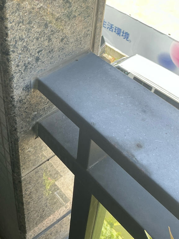 台北舊大樓欄杆生鏽更換前的現勘細節，照片聚焦金屬橫桿靠近外牆磁磚的交接位置，可看見原有欄杆與建築立面相接的構造。正邦鍛造評估不鏽鋼玻璃欄杆更換時，須確認牆面固定位置、舊有接合狀態及拆換空間，不能只依欄杆外觀判斷施工方式。