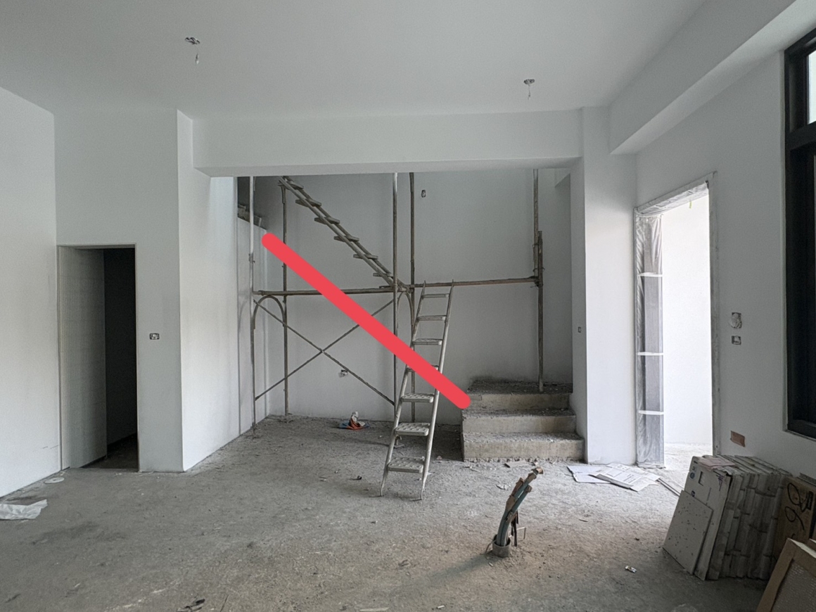 南投龍骨梯工程施工前的住宅室內全景，現場仍為裝修中的水泥地坪，後方有既有混凝土平台與施工鷹架，照片上以紅色斜線標示預定樓梯方向。這張紀錄可協助理解龍骨梯位置需與既有平台、牆面及室內動線整合，實際踏階尺寸、結構固定方式與欄杆高度應依現場丈量和設計確認。